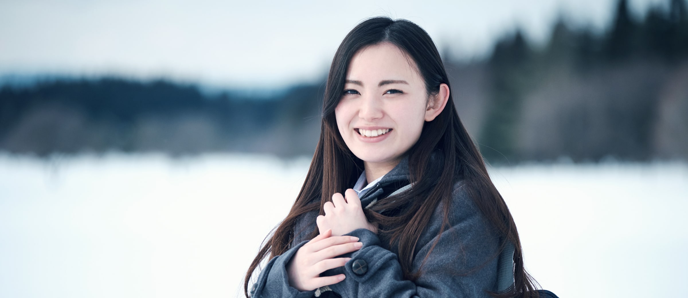写真：雪景色の中、コートを着た女子学生が笑顔でこちらを見ている